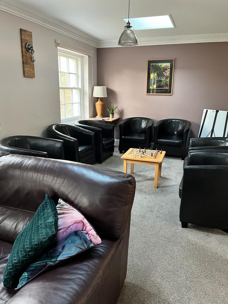 Alpha phase group room - a room with black armchairs centred around a coffee table. There's a large window and wall wall is painted a dusky pink colour