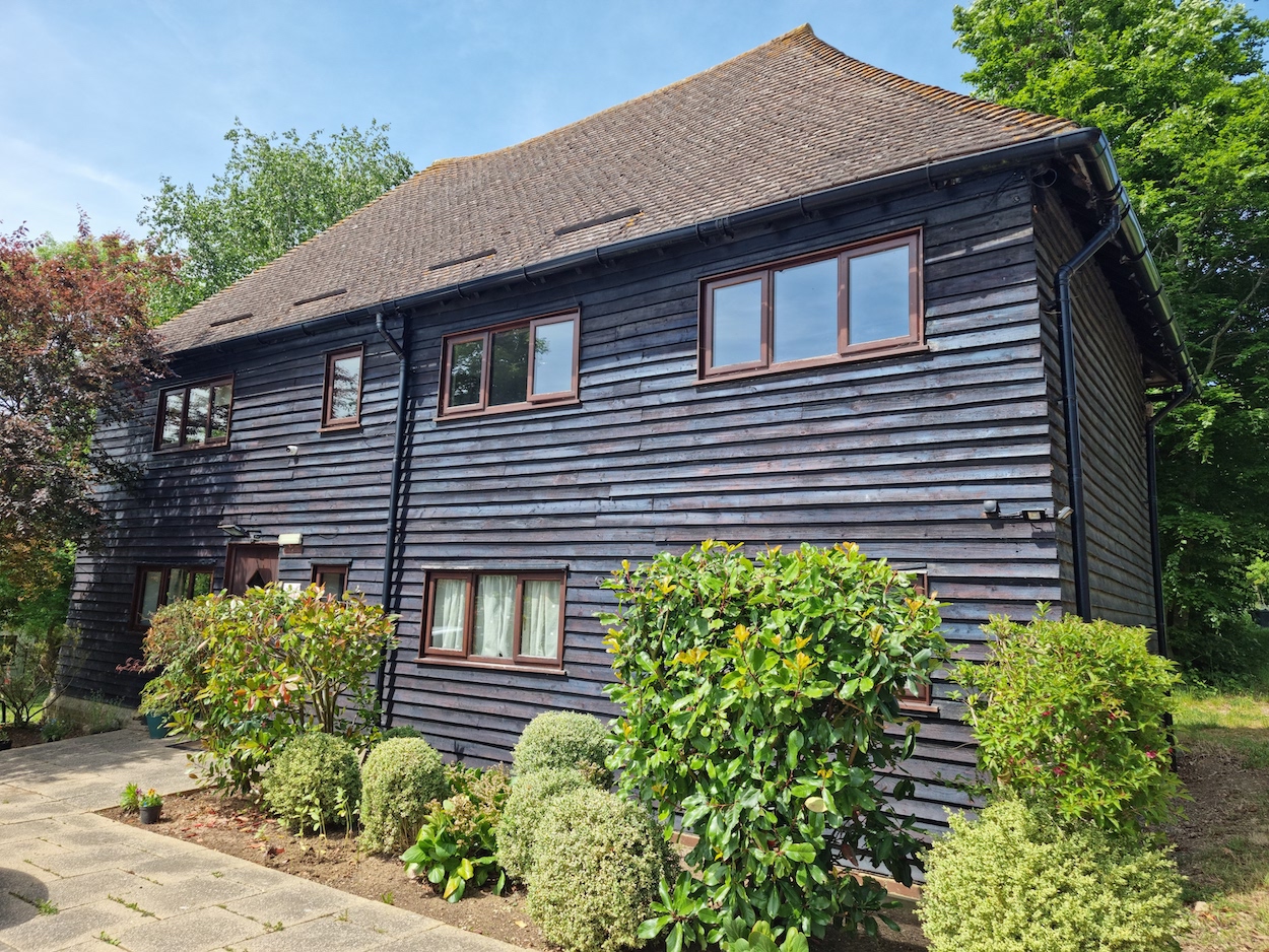 Kenward Trust - a converted barn with dark grey wood. There are hedges in the foreground