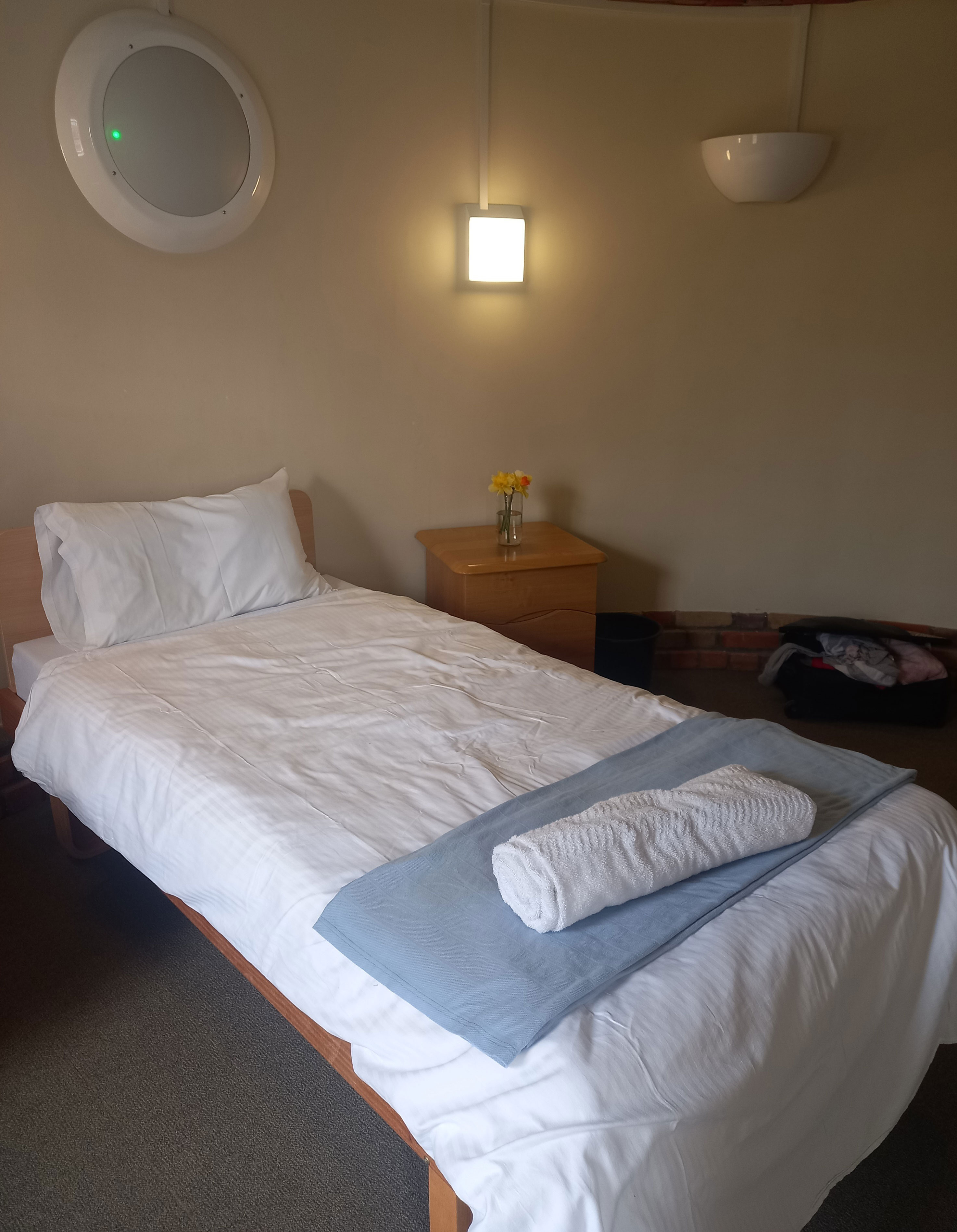 Bridge House Bedroom - a white single bed in a room with white walls. Towels are laid out on the bed