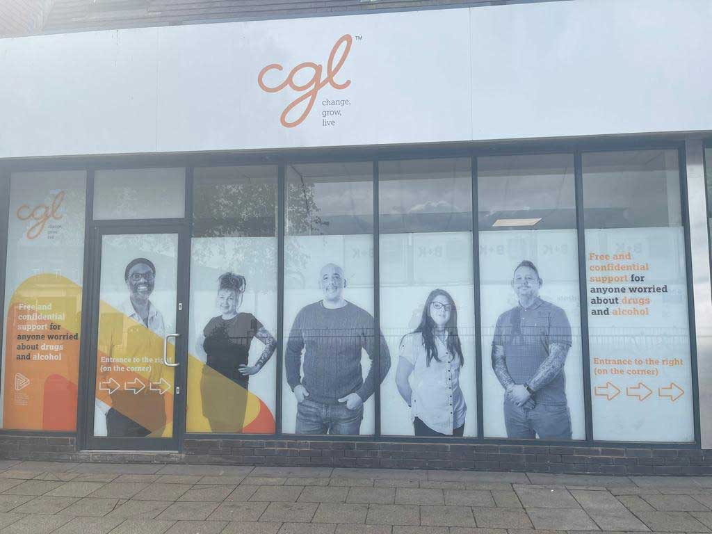 Outside of the Crew building - a white banner says 'CGL' in orange, and the windows have decals of photos of people in them. Each window has a different person