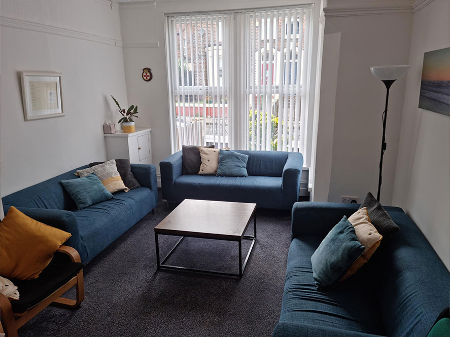 A group room - there are three blue sofas centred around a coffee table, white walls and large windows.