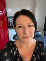 A photo of a women with dark hair pulled back from her face. She is wearing a black blouse with flowers