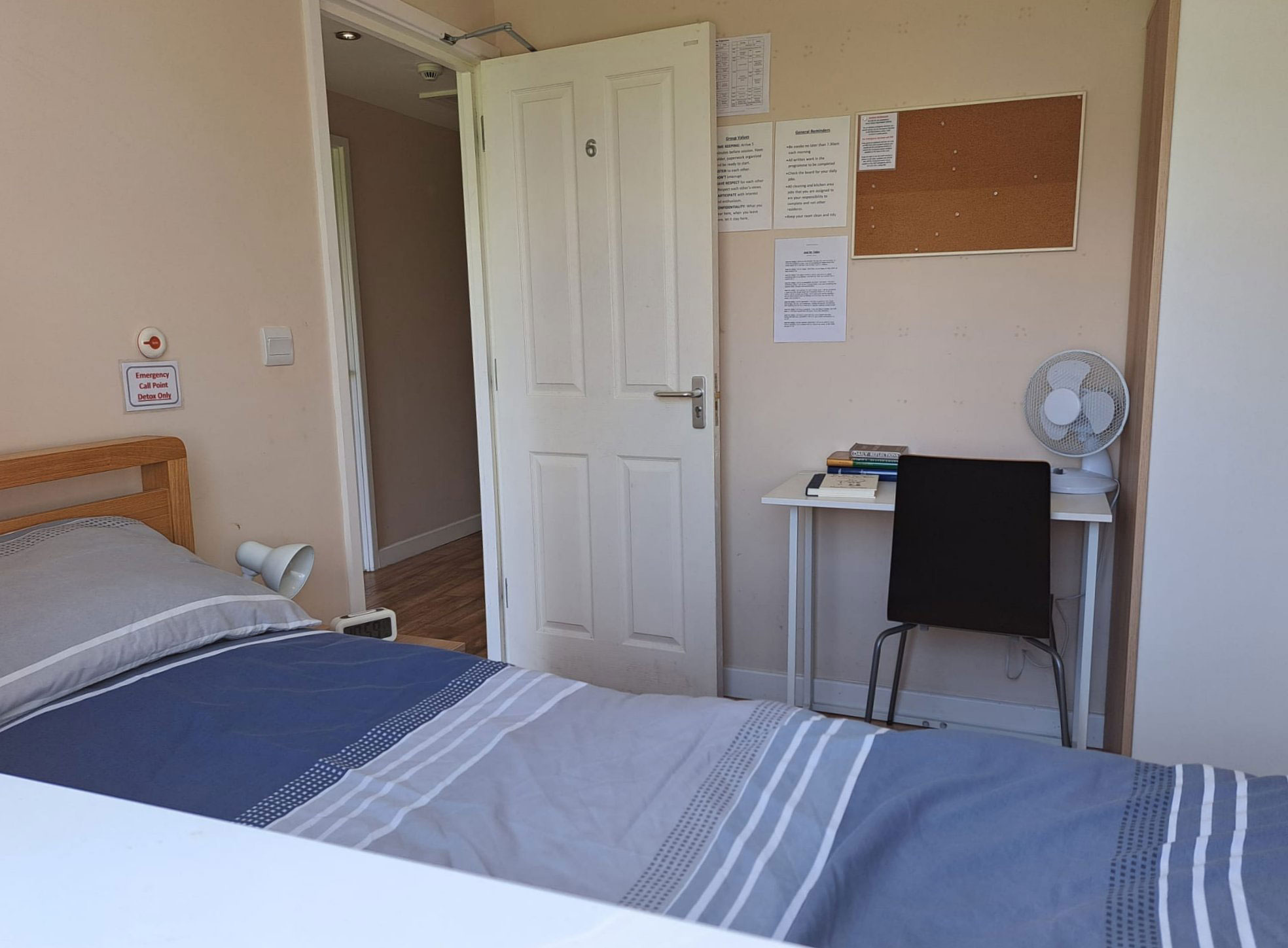 ESH community - bedroom. A blue single bed in a room with white walls, a desk with a black chair and a cork noticeboard