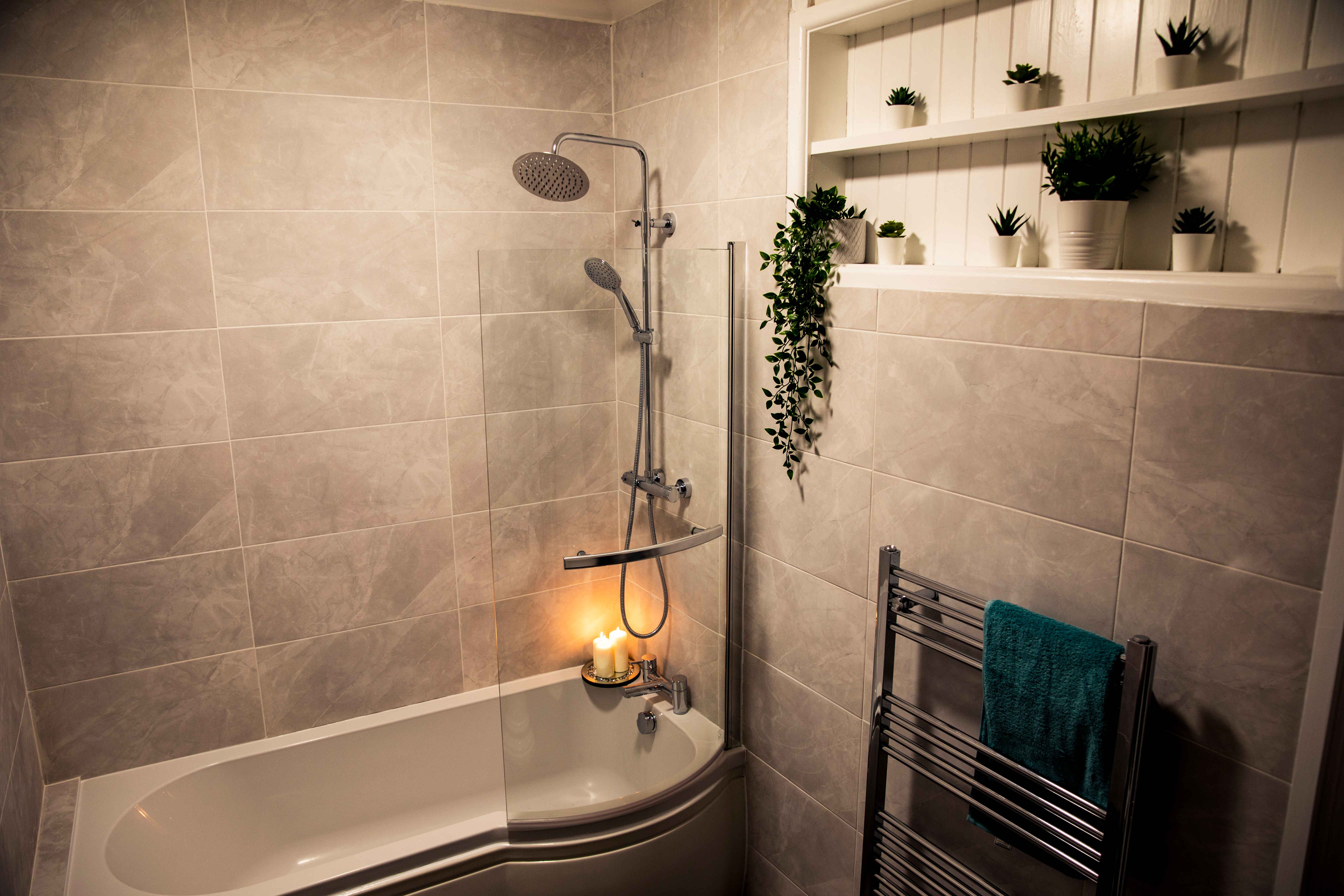 A bathroom - the walls are covered in marble tiles, there is a bathtub and a shower head attached to the wall.