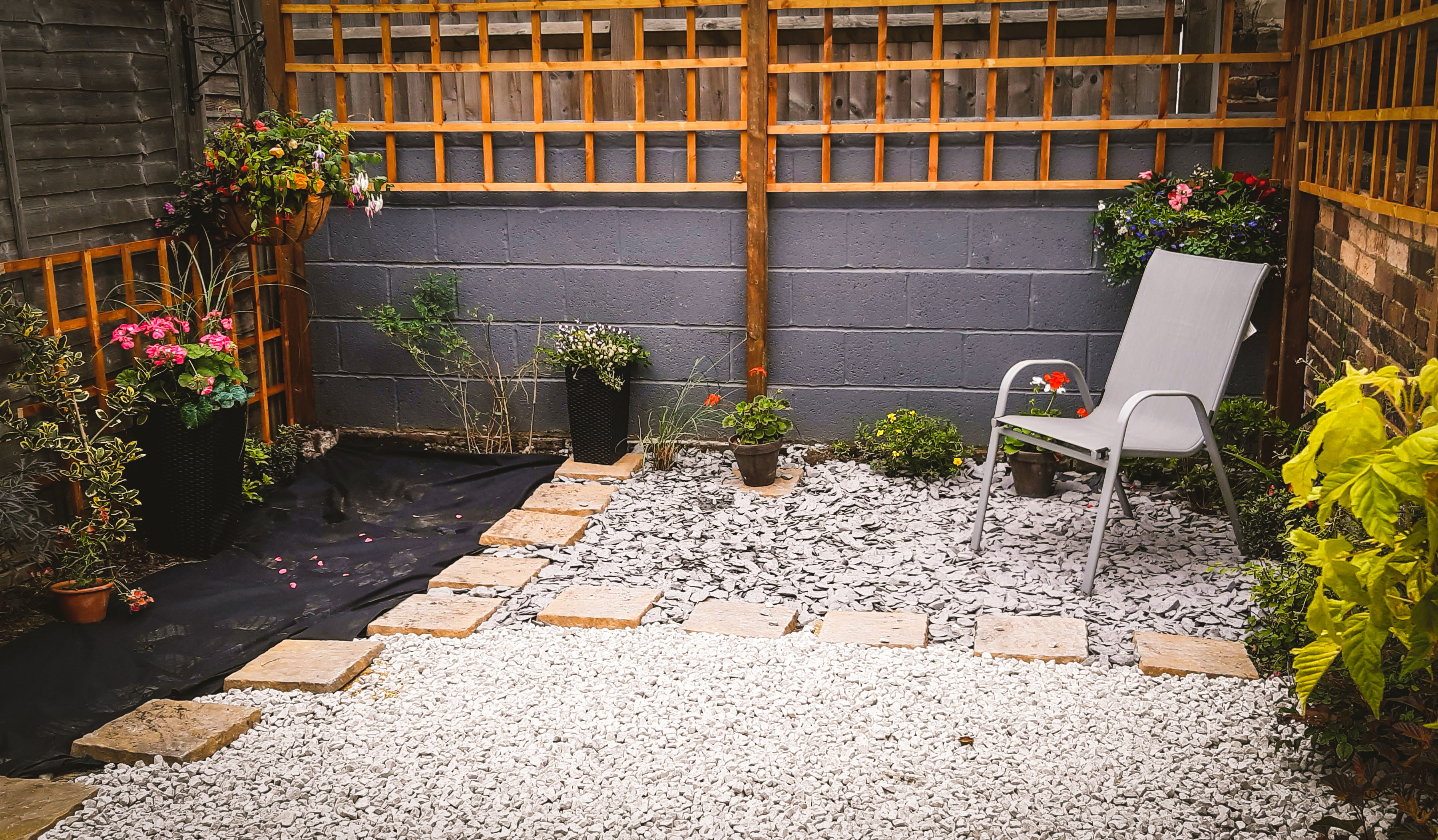 A garden with plants around the edge, a garden chair in the corner and gravel spread across the floor.