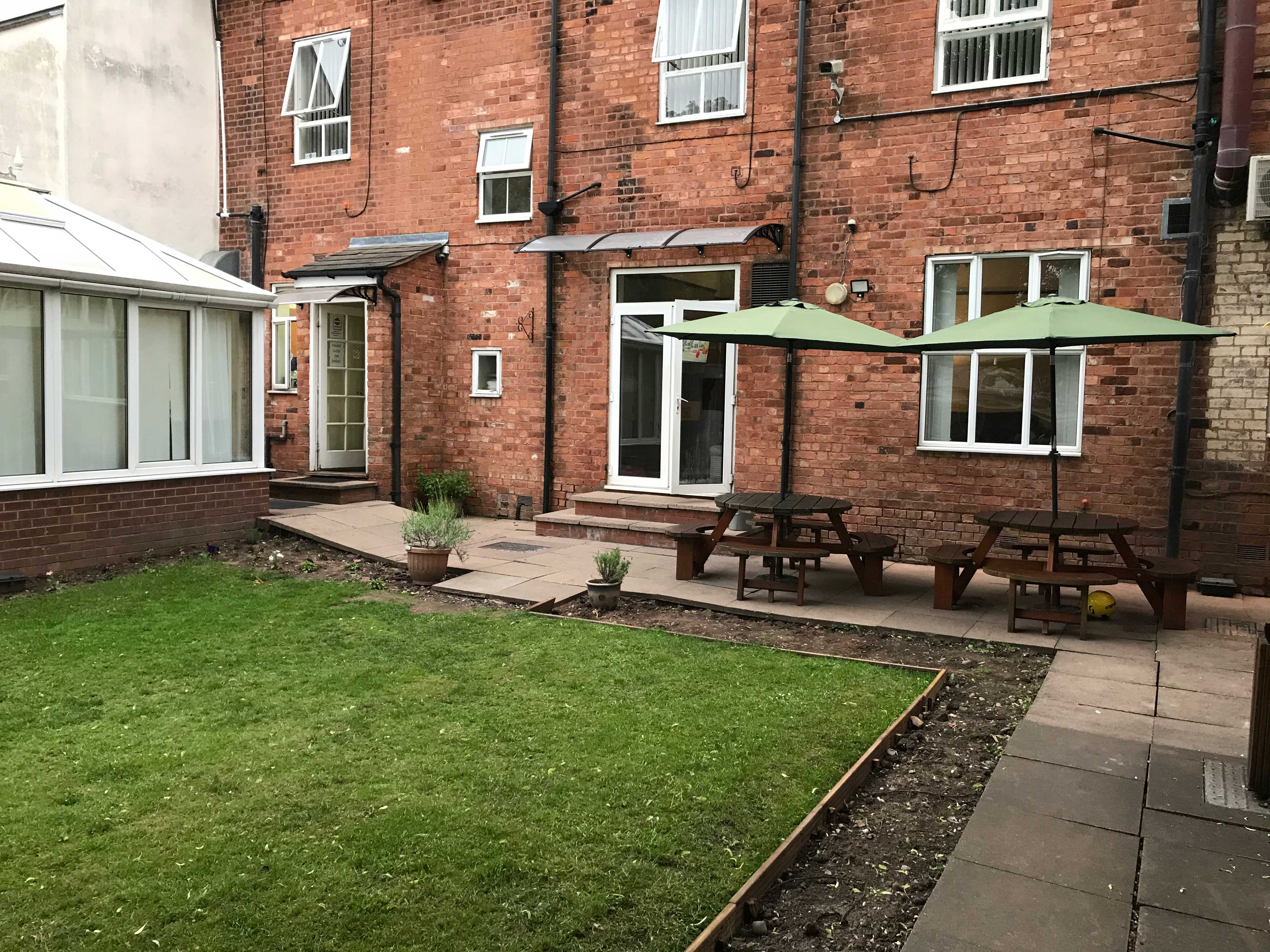 A garden with a conservatory and two wooden picnic benches.