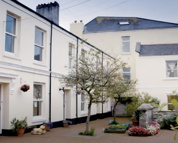The outside of a white painted building. It has a courtyard with a few trees around it