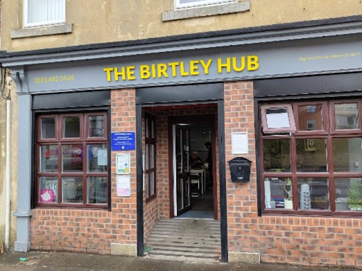 The outside of a red brick building. There are two windows either side of the door and a sign above that reads The Birtley Hub