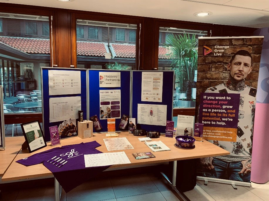 A stall with posters around it and items scattered across the tables such as t-shirts, pens, paper