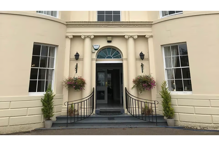 Front door to a white walled manor house with columns either side of the door and big windows