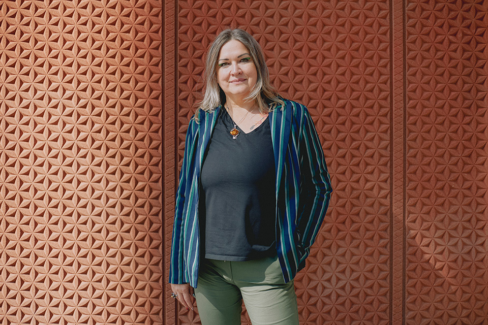 Aldona stands in front of a textured terracotta wall looking to the camera with a gentle smile