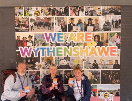 Three people stood in front of a photo collage with the words We Are Wythenshawe