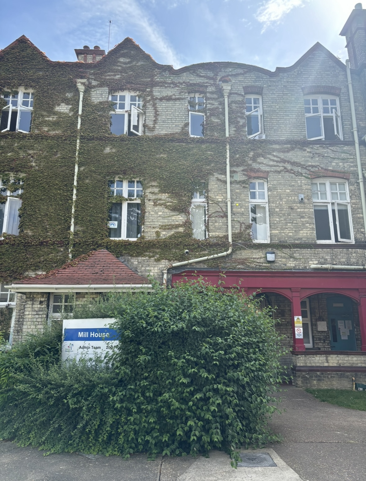 The outside of a building with ivy growing on it and red arches that make up the entrance