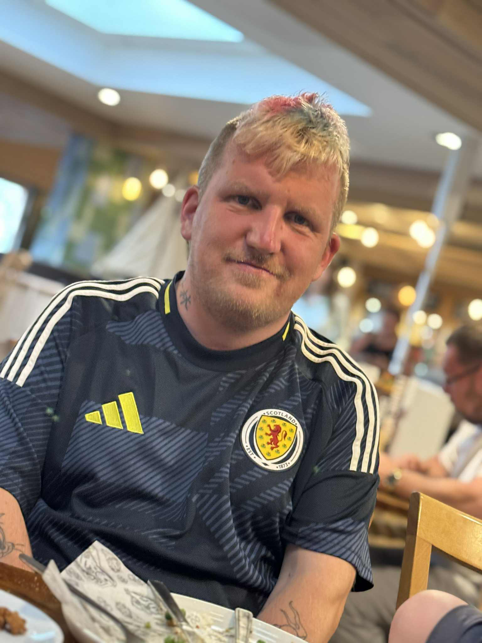 Colin has short blond hair and is wearing a football shirt