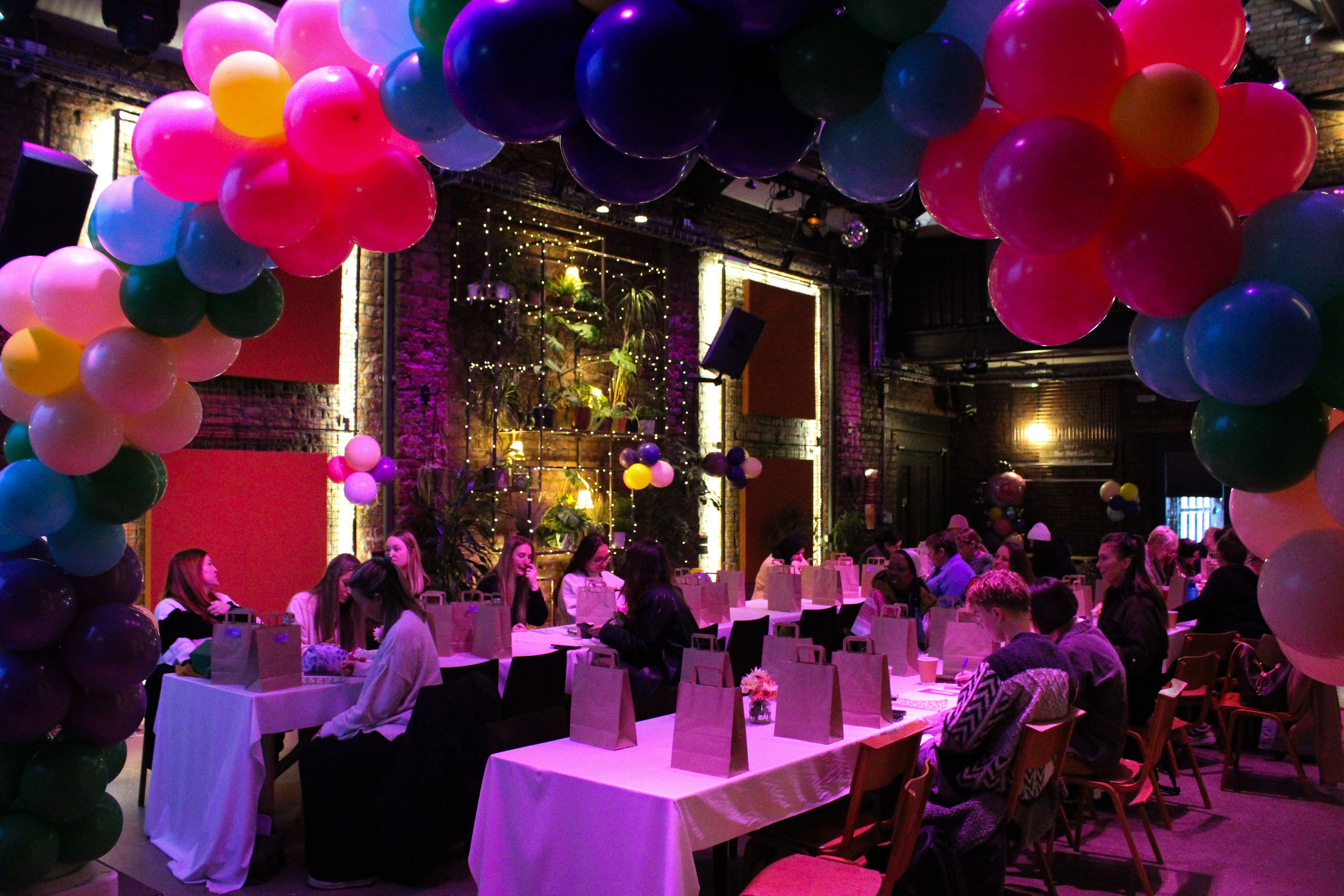 A room with people sat at tables with balloons scattered around