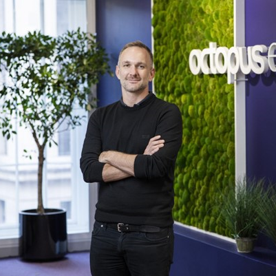 Jon Paull stands in an office with an Octopus Energy sign in the background