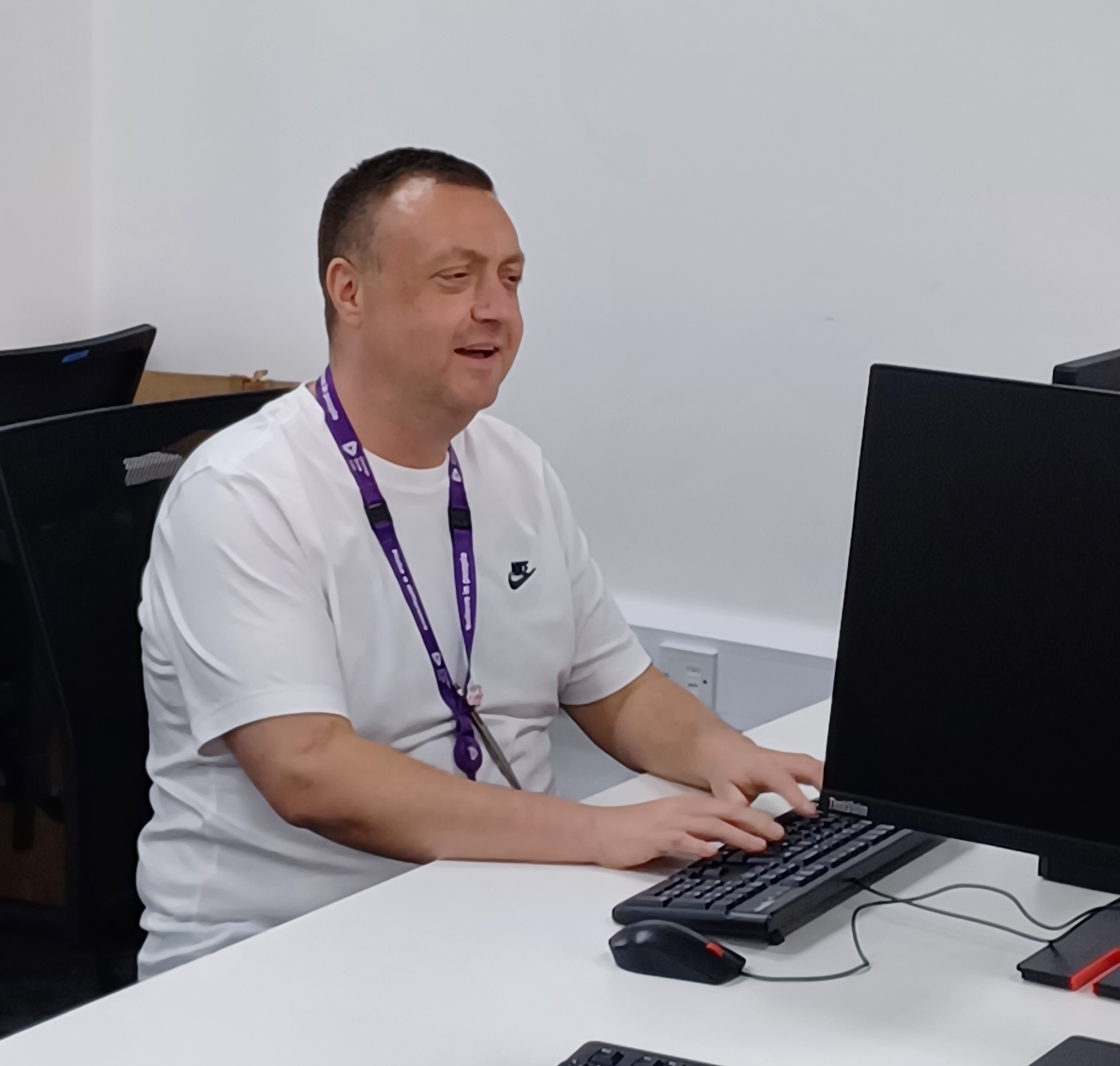 An image of a man in a white t-shirt typing at a computer