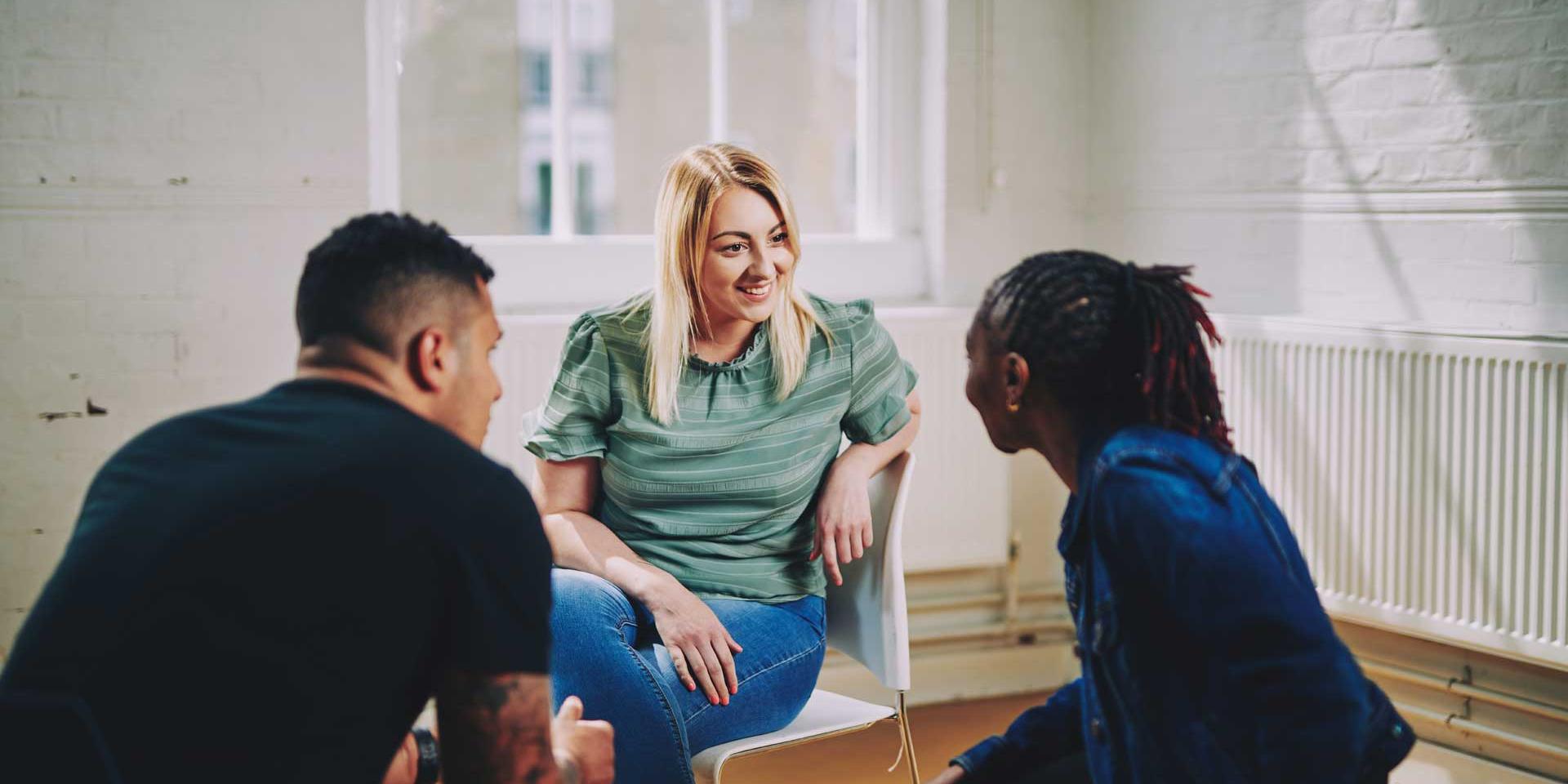 woman smiling sitting on a chair talking to two people