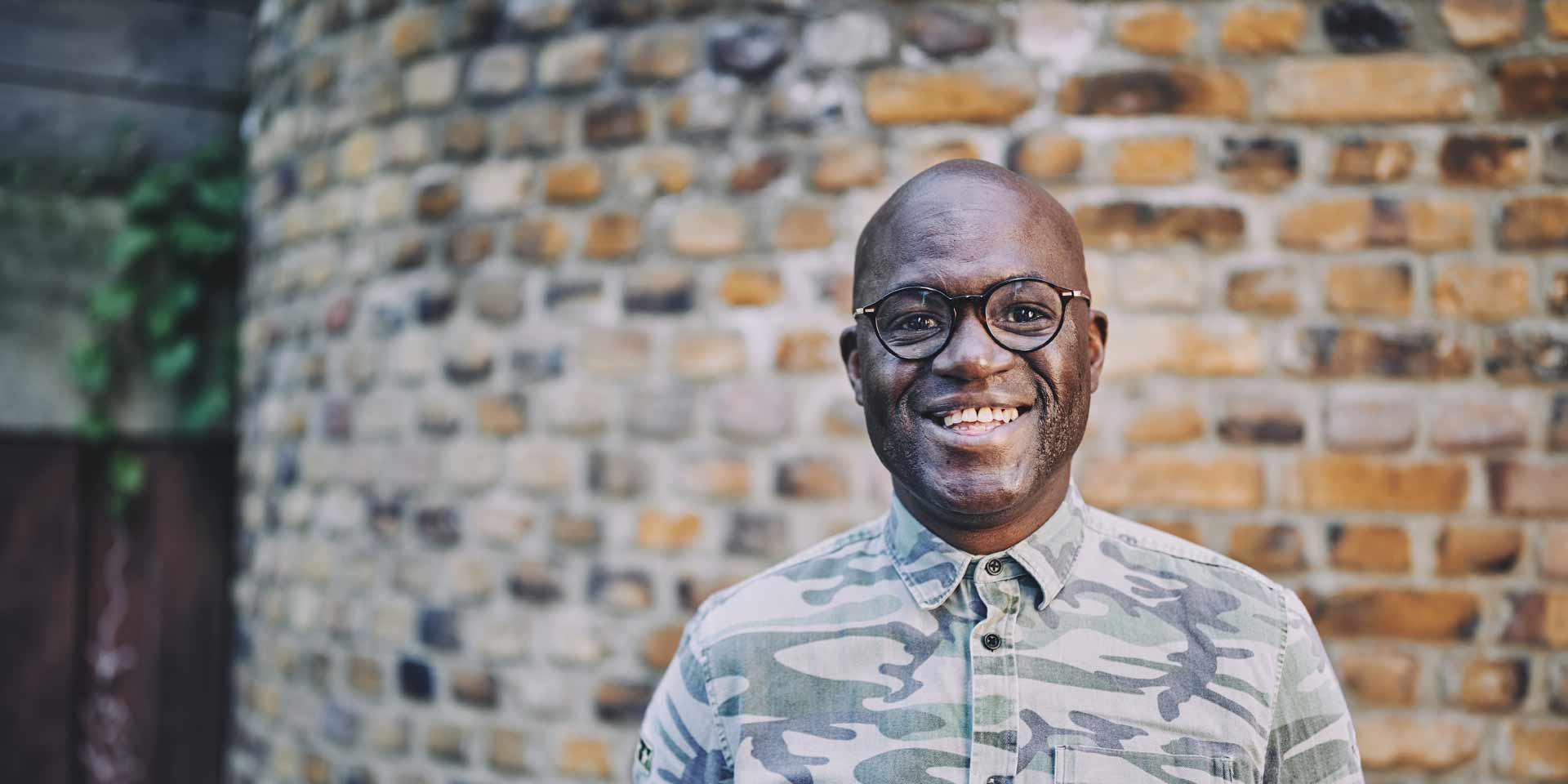 man smiling standing in front of a brick wall