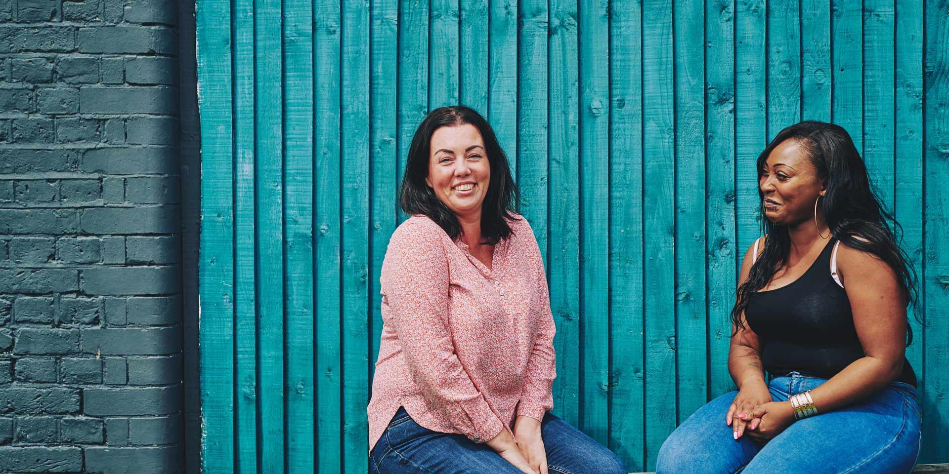 two women sitting on a bench talking and smiling