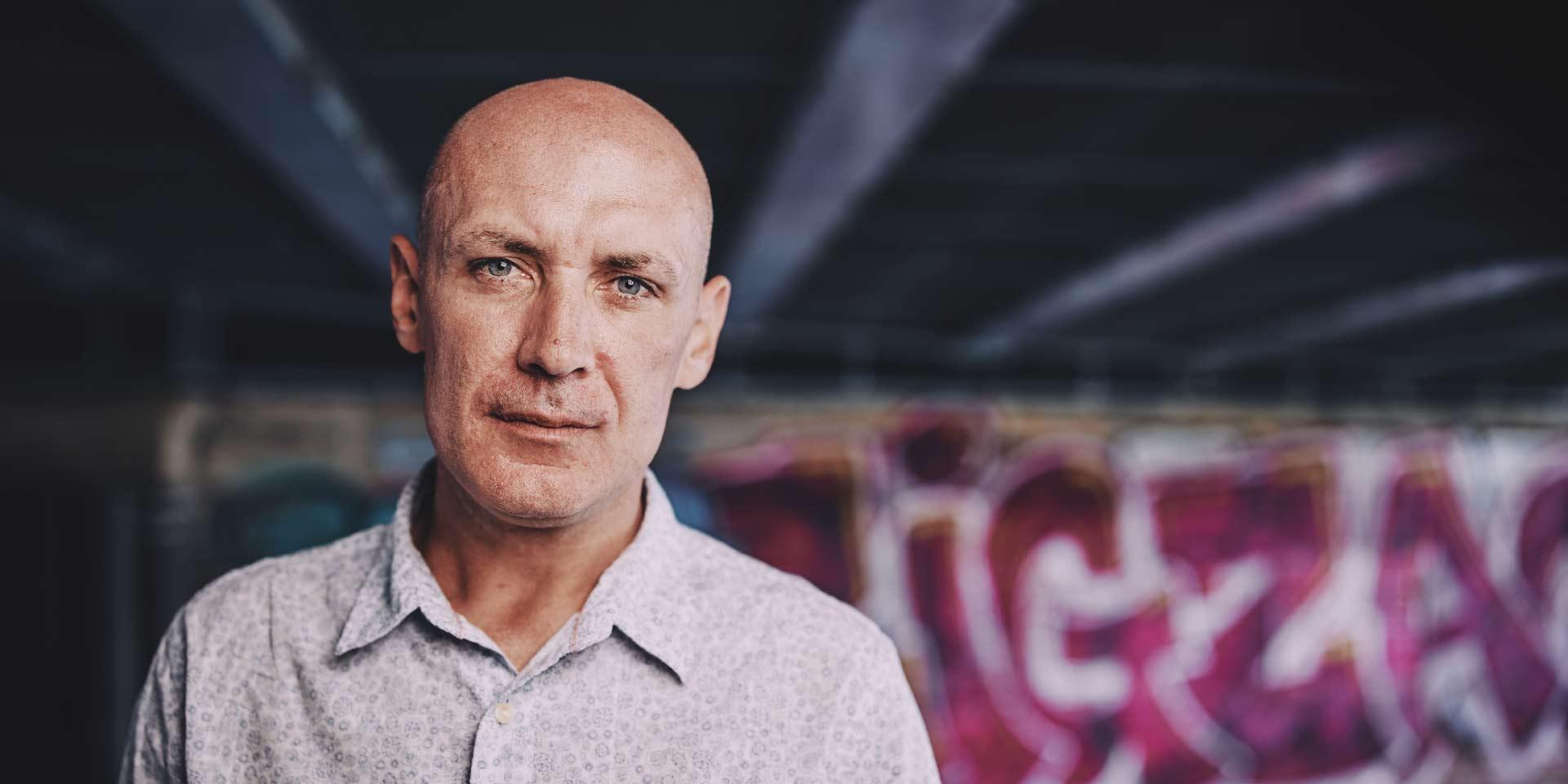 man standing in front of some graffiti under a bridge