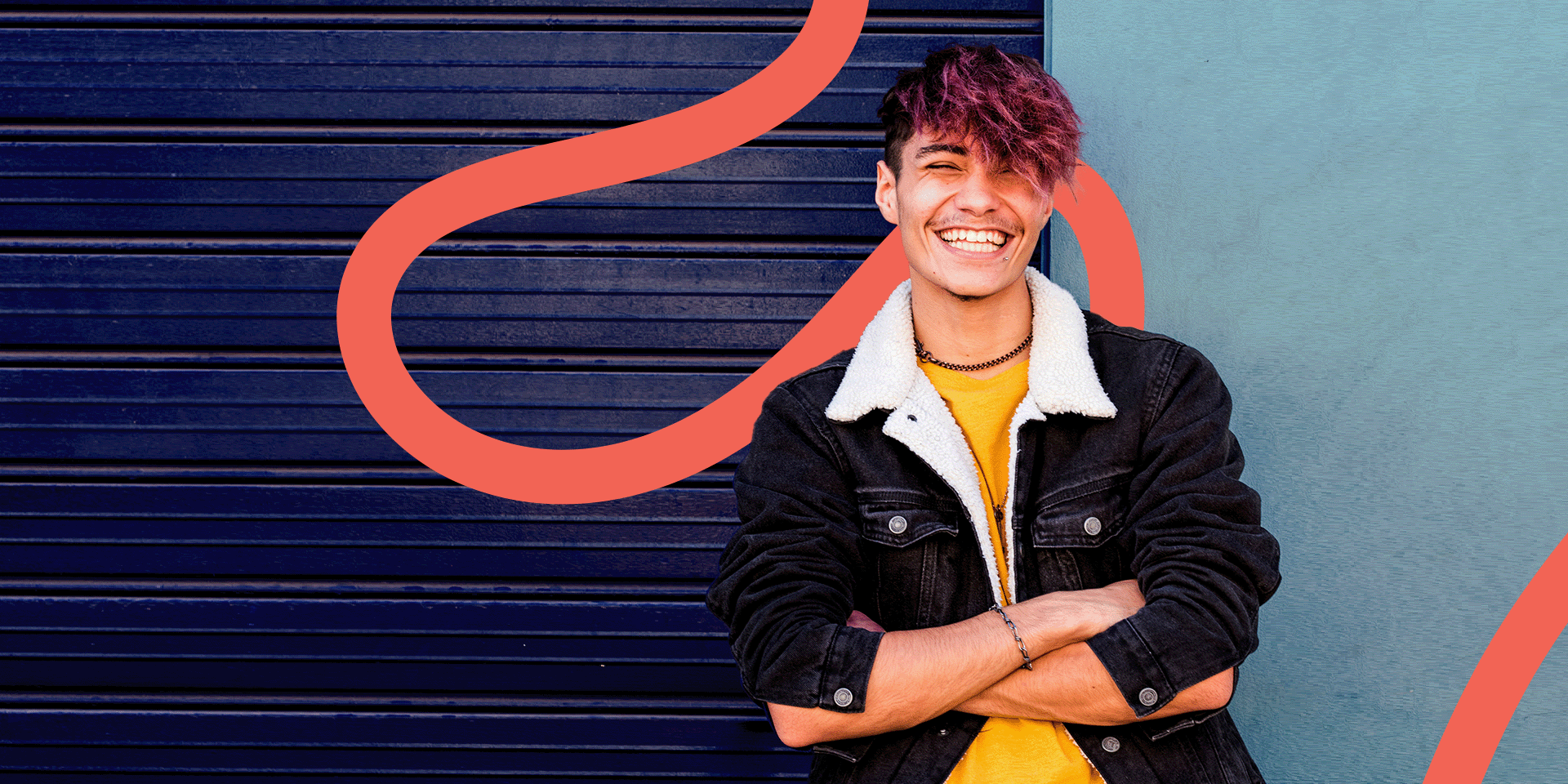 Young person stands in front of a wall with arms folded smiling broadly