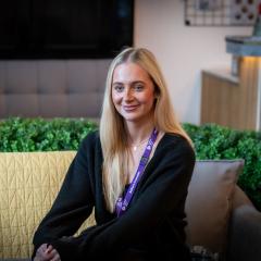 A young blonde woman sitting on a sofa looking at someone off camera