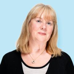 Sue has shoulder length blonde hair and is wearing a black and white striped top with a black cardigan