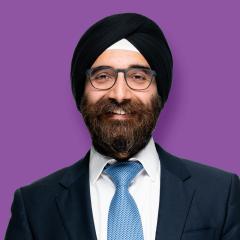 Dr Prun is wearing a black suit jacket, light blue tie, white shirt. He has a beard and glasses. He is wearing a black turban