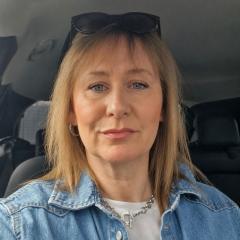 Rachel has shoulder length blonde hair and is wearing a white top and light denim jacket