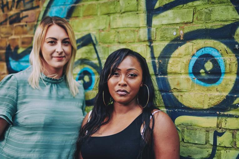 two women standing in front of a wall with graffiti