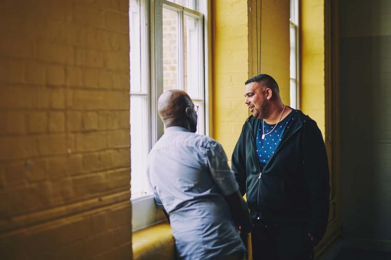 Two men are having a conversation by a window