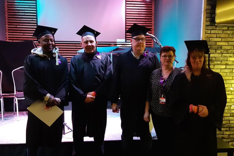 Four graduate and staff members standing together to pose for a photo at Kings Church Hub in Gateshead as they celebrate their graduation ceremony