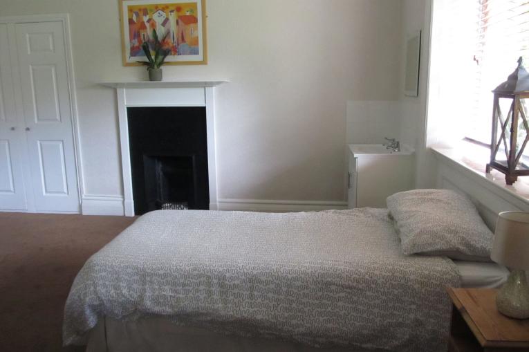 A bedroom  with white walls, a window and a single bed with white sheets