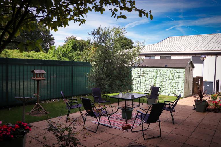 A back garden with a shed in the corner, with a table and chairs on a patio