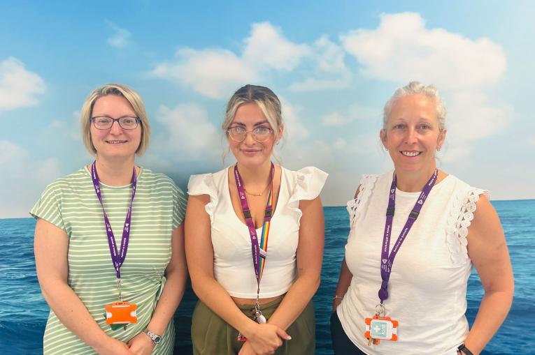 Three women stood in front of a backdrop of the ocean