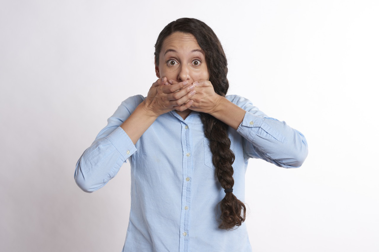 A woman with long hair in a plait holding her hands over her mouth