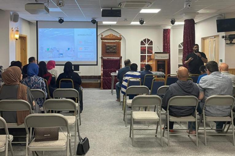 People sitting on chairs and listening to a presentation as part of one of the mosque sessions