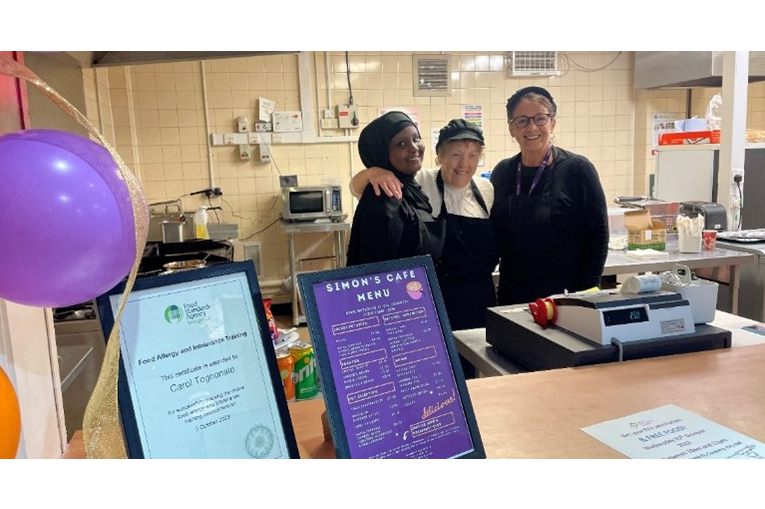 Three people stood behind a counter. On the counter is a menu and purple balloons