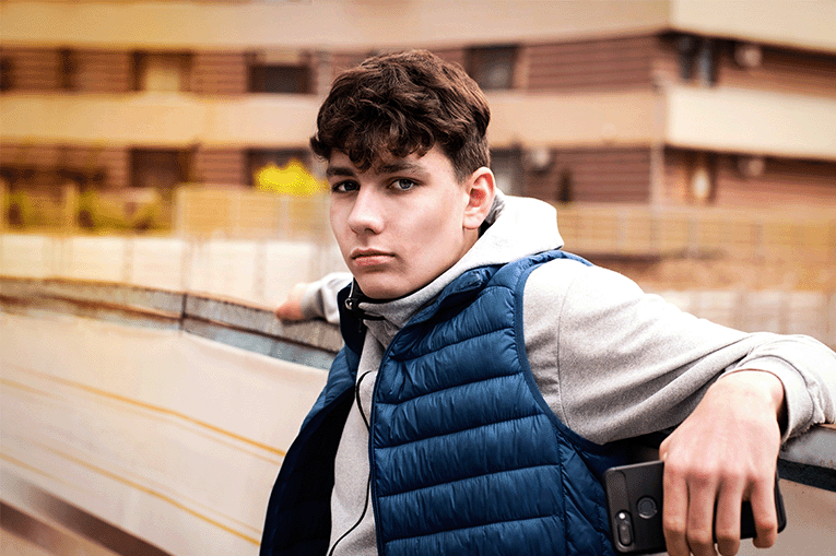 a young man in an urban housing setting looking solemnly direct to camera