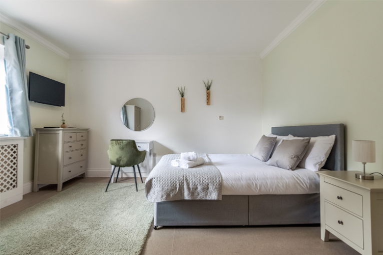 A large bedroom with double bed, desk, drawers, and TV mounted on the wall