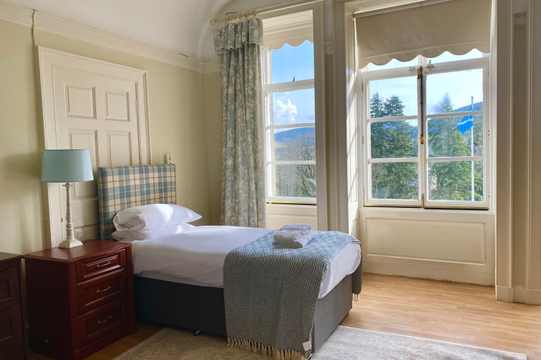 A single bed with bedside table and large windows