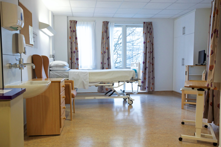 A hospital room with double doors leading out to a garden
