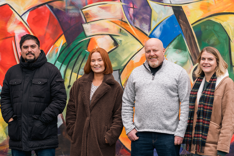 2 women and  men stood in front of a wall of graffiti smiling at the camera