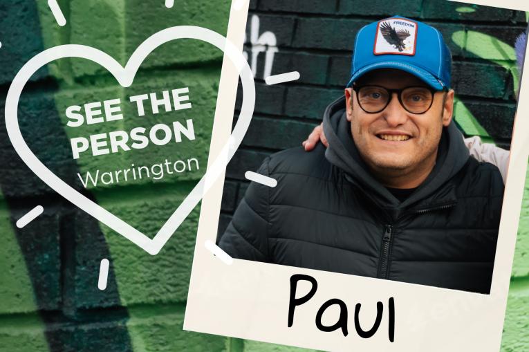 A colourful wall background with a heart stamp on the left with the words See The Person Warrington inside the heart. On the right is a polaroid photo with a man wearing a blue baseball cap and black coat. The name Paul is at the bottom of the polaroid.