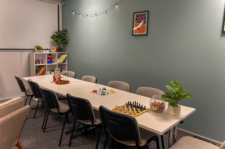 A long table with different board games on top and a cabinet with toys in the corner of the room