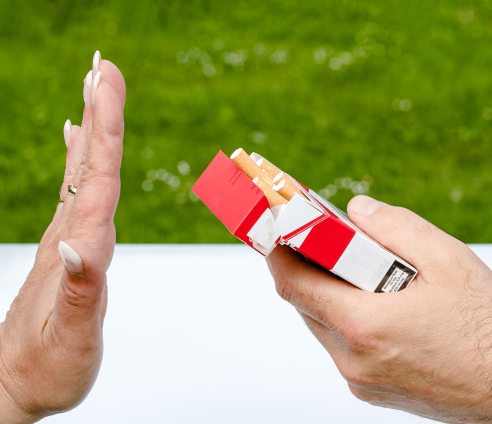 A hand holding a packet offering a packet of cigarettes and another hand saying no