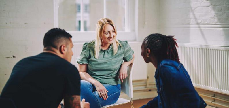 woman smiling sitting on a chair talking to two people