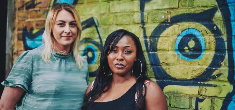 two women standing in front of a wall with graffiti