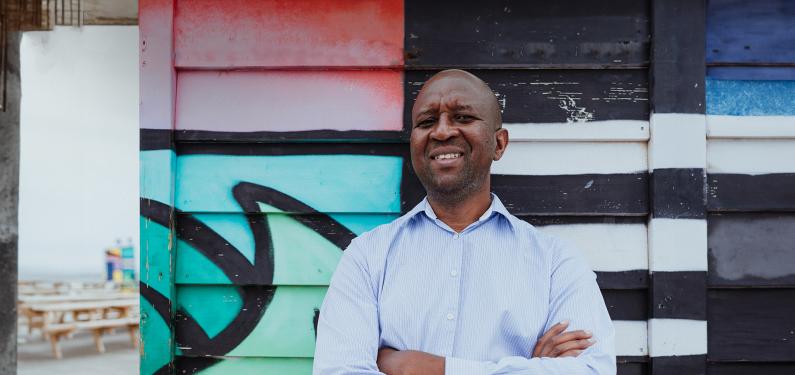 A person smiling at the camera with a mural in the background